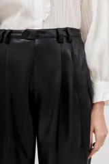 Pantalón estilo capri de efecto cuero negro, con corte holgado y detalles de costuras geométricas en la parte delantera.