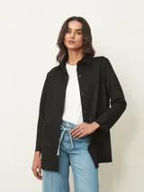 Sobrecamisa negra de corte recto y largo medio, con cuello clásico, cierre frontal de botones y dos bolsillos frontales aplicados.