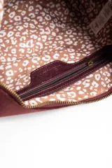 Cartera tipo bandolera de gamuza sintética color bordó, con diseño de flecos largos en la parte inferior y correa ajustable con nudo lateral. Incluye cierre superior y detalle de placa metálica con logo.