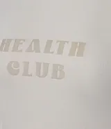 Remera deportiva color beige con cuello redondo, mangas cortas y estampado en relieve con la frase "Health Club". Confeccionada en poliamida texturizada con tecnología Dry que facilita la evaporación del sudor.