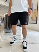 Bermuda de jogging color beige, con bolsillos laterales y estampa con texto blanco en la pierna izquierda.