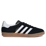 Championes Adidas Gazelle Indoor de diseño clásico, confeccionados en gamuza negra con las icónicas tres tiras laterales en blanco. Presentan el nombre del modelo en letras doradas, talón en contraste blanco y suela de caucho color caramelo.