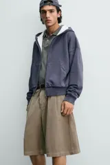 Bermuda wide fit color beige, confeccionada en pana de algodón. Presenta pliegues frontales en la cintura, bolsillos delanteros y bolsillos traseros de plastrón. Cierre frontal con cremallera y botón.