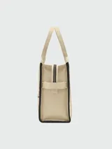Bolso tipo tote de gran tamaño en color beige, confeccionado en lona resistente. Presenta el logo estampado en negro en el frente y detalles de cintas laterales con inscripciones. Cuenta con doble asa superior para llevar al hombro.