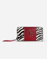 Billetera rectangular con cierre perimetral, confeccionada en una combinación de cuero con estampado animal print de cebra y una franja central de cuero rojo con apliques de tachas metálicas. Incluye un tirador de cierre con flecos rojos.