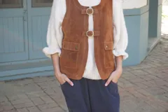 Chaleco de cuero gamuzado color marrón, con cierre frontal mediante dos hebillas metálicas y dos bolsillos frontales con solapa.