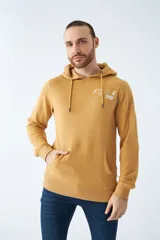 Buzo canguro color mostaza con capucha ajustable mediante cordones, bolsillo frontal tipo canguro y estampado gráfico en el pecho. Presenta puños y ruedo acanalados.