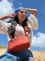 Bandolera de diseño moderno y funcional, confeccionada en nylon color marrón claro. Cuenta con múltiples compartimentos con cierre metálico, herrajes plateados y una correa ancha ajustable con detalle de marca.