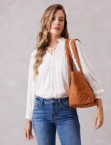 Bolso tipo tote de diseño capitoneado en color marrón, con doble asa para llevar al hombro y cierre mediante botón metálico. Cuenta con forro interno a tono y bolsillos organizadores en su interior.