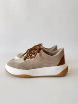 Championes de cuero color visón con cordones marrones, suela blanca y base color caramelo.