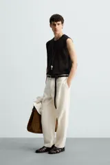 Chaleco de punto negro, con cuello redondo y manga sisa, confeccionado en tejido con estructura abierta (calado). Presenta bajo con aberturas laterales y acabados en rib.