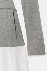 Vestido midi de cuello redondo y manga larga, con la parte superior gris y la falda blanca. La parte superior presenta un detalle de tejido superpuesto ajustable con lazada en la cintura. La falda es de tipo gabardina.