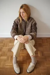 Chaqueta bomber color bordó con mangas de cuero sintético marrón y cuerpo de tweed con patrón de espiga. Cierre frontal con botones a presión y cuello redondo.