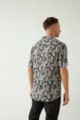 Camisa de manga corta con cuello cubano, confeccionada en viscosa con estampado de hojas en tonos azules. Presenta cierre frontal abotonado y corte slim.