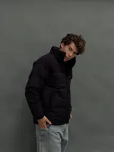 Campera puffer negra con diseño de paneles, cierre frontal completo y cuello alto. Presenta una textura diferenciada en la parte superior y bolsillos laterales.