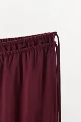 Pantalón bordó de tiro medio, confeccionado en mezcla de viscosa y lino, con pernera recta y amplia, y detalle de doble cintura ajustable con lazadas.