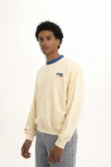 Buzo color crema de corte holgado, con cuello redondo y puños acanalados en color azul. Estampado pequeño con la frase "Karma Club" en el pecho.