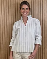 Blusa blanca con rayas verticales finas negras, cuello alto con volados y escote en V, manga larga y corte holgado.