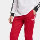 Pantalón deportivo Adidas de corte ajustado, color rojo con las icónicas tres tiras blancas laterales y logo del trébol bordado en la parte superior. Confeccionado en tejido de piqué con cintura elástica y cordón de ajuste.