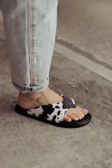 Sandalia tipo flip-flop con estampa cow print en blanco y negro. Presenta una tira ancha acolchonada que abraza el pie y una base negra lisa. Diseño liviano y cómodo de la marca Anne Chaussure.