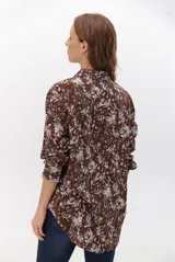 Camisa de corte holgado con estampado floral en tonos marrones y blancos, cuello clásico y cierre frontal con botones.