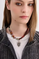 Choker con cadena de piedras y piezas circulares de diferentes tamaños y tonos, incluyendo cuentas rojas, naranjas, lilas, verdes y negras. Presenta detalles de púas doradas y un dije central en forma de escudo de metal grabado.