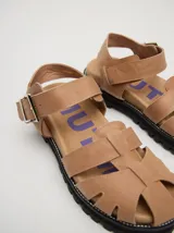 Sandalias romanas de cuero tostado, estilo chunky con plataforma y suela tractora de goma negra. Cuentan con tiras cruzadas en el empeine y tira ajustable con hebilla metálica en el tobillo.