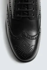Zapato tipo derby de hombre, color marrón oscuro, fabricado en piel con detalles de picados (brogue) en puntera y laterales. Posee plantilla interior de piel y suela track con ligero tacón.
