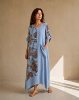 Vestido largo celeste con gran estampado floral marrón en un lateral, de corte holgado, mangas cortas con vuelta y un bolsillo de parche frontal.