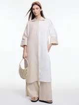 Vestido camisero largo confeccionado en 100% lino, con manga 3/4 y silueta relajada. El diseño juega con bloques de color en contraste, combinando blanco y beige.