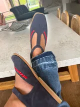 Ballerinas de gamuza color marrón oscuro con diseño tipo T-strap y detalles de costuras decorativas en color verde oliva. Cuentan con cierre de pulsera al tobillo y suela plana.