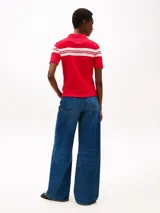 Chomba roja de piqué de algodón elástico con corte slim, cuello clásico, tapeta de seis botones y rayas horizontales blancas en el pecho y mangas. Logo de Tommy Hilfiger bordado en la manga.