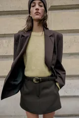 Falda pantalón corta de tiro medio color beige claro, con cierre frontal y detalle de cinturón negro con hebilla metálica redonda dorada.