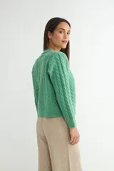 Cardigan de punto gris con diseño de ochos y trenzas, cuello redondo y cierre frontal con botones dorados grandes. Posee mangas largas con puños acanalados.