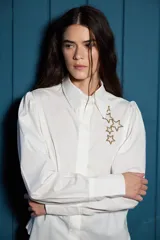 Camisa de corte clásico color blanco, con mangas largas abullonadas en los hombros y puños abotonados. Presenta un detalle de estrellas bordadas en color dorado sobre el lado izquierdo del pecho.