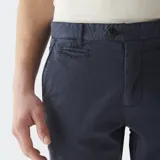 Pantalón chino color beige, de corte recto, con bolsillos laterales y traseros. Se ajusta a la cintura con cinturón de cuero marrón.