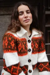 Saco tejido a mano con diseño jacquard en tonos rojo, naranja y marrón. Presenta cuello tipo polo, cierre frontal con botones grandes, mangas largas y tajos laterales en el ruedo.