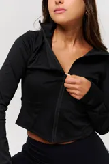 Campera deportiva negra de corte crop, con cierre frontal completo y cuello alto. Confeccionada en tejido técnico elástico, presenta costuras reforzadas que realzan la silueta.