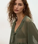 Blusa de tul transparente color verde oliva, con diseño de volados en el frente, escote en V con lazo y borlas decorativas, y mangas largas amplias con puños elásticos.