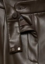 Pantalón wide leg de efecto piel color marrón, con tiro medio, bolsillos laterales, pinzas delanteras y cierre frontal con botón, gancho y cremallera ocultos. Cuenta con forro interior.