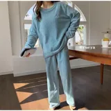 Conjunto de pijama de dos piezas confeccionado en tela de plush texturizada con diseño de rayas verticales en relieve. Incluye una remera de manga larga con cuello redondo y un pantalón de corte holgado. La remera presenta un pequeño bordado decorativo en el pecho.