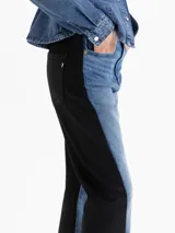 Pantalón de jean con diseño bicolor, presentando el frente en denim azul lavado con efecto vintage y los laterales y parte trasera en tejido engomado negro. Posee silueta recta tipo mom fit y tiro medio.