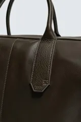 Bolso shopper de cuero vacuno con acabado abatanado, diseño minimalista con cierre de cremallera superior, doble asa de mano y detalle de llavero colgante. El interior incluye un bolsillo plano y un bolsillo con cierre.