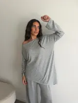 Conjunto gris melange compuesto por un buzo de cuello bote amplio y corte asimétrico con bolsillos, y un pantalón largo de corte recto y holgado.