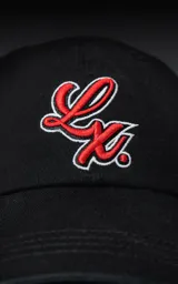 Gorra de gabardina color negro con visera curva y bordado frontal en hilo rojo con borde blanco que simula una letra 'L' estilizada. Posee ajuste trasero de velcro.