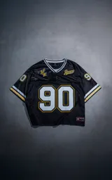 Camiseta estilo jersey de fútbol americano en color negro con detalles en amarillo y blanco. Presenta el número 90 en el frente y en las mangas, con inscripciones bordadas en el pecho y cuello en V con franjas decorativas.