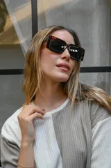 Lentes de sol con montura gruesa de forma cuadrada/rectangular, color verde oliva translúcido, y cristales tintados en tono ámbar/marrón claro.