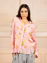 Camisa de manga larga color rosa con estampado de soles, lunas y flores en tonos amarillos y naranjas. Tiene cuello clásico y cierre frontal con botones.