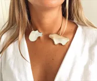 Gargantilla rígida dorada con apliques de nácar irregulares en los extremos.