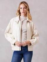 Campera bomber de eco cuero color beige, con cuello camisero, cierre frontal metálico y bolsillos delanteros con solapa y botón a presión. Presenta mangas largas con puños abotonados y ruedo trasero elastizado.